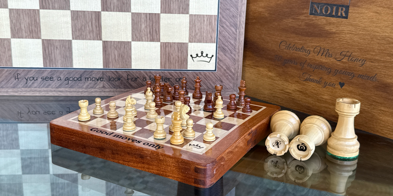 Laser-engraved text on a chessboard border and a storage box, with initials engraved on top of the rooks